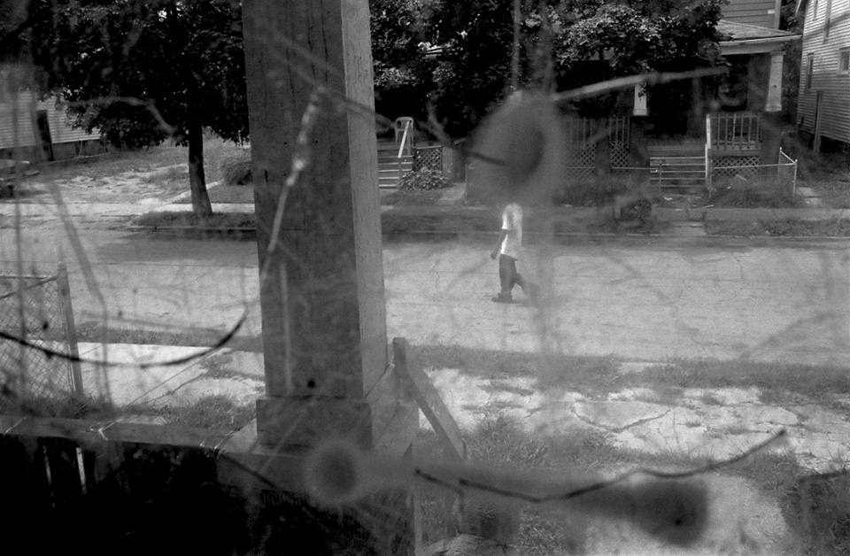 person walking down street as seen through window with bullet holes.