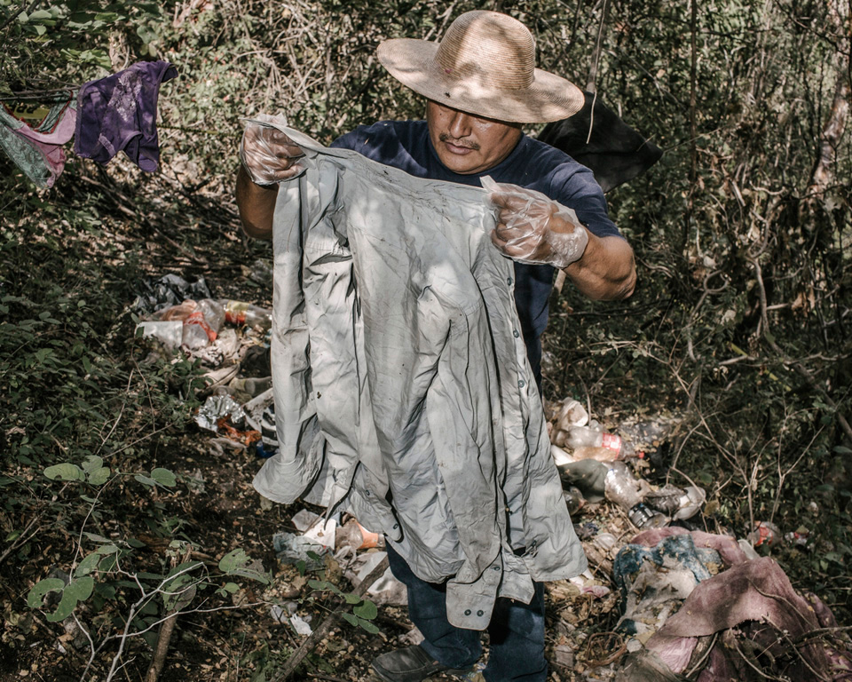 These belongings and trash were found near a grave that was found outside of Iguala soon after the 43 students disappeared. At first authorities suspected the graves contained the students but DNA confirmed that none of the 28 bodies belonged to the students shedding light on the years of disappearances that have plagued Iguala. Here Miguel holds up a "Manchester" brand shirt in good condition.