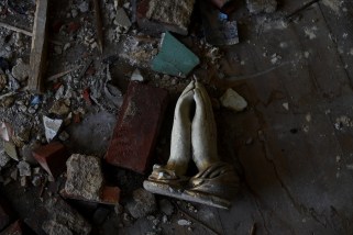 Broken statue of hands in prayer over a dark background. 