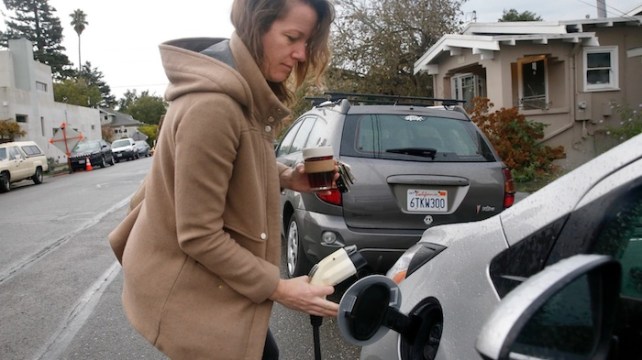 A white woman putting a portable charger into her car in front of her home