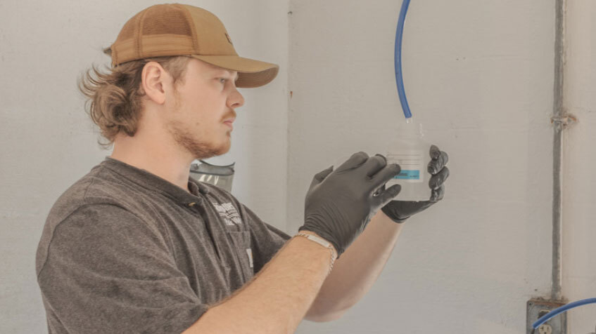 White man with light copper hair and tan baseball cap holds a plastic container of water.