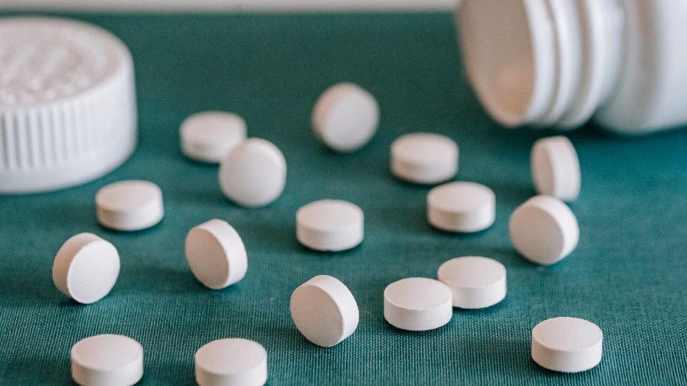 White pills laid out on a turquoise counter with a white bottle in the background