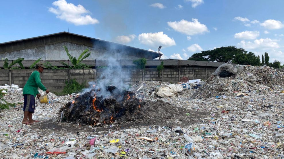 Man wearing a green shirt and jeans burning plastic