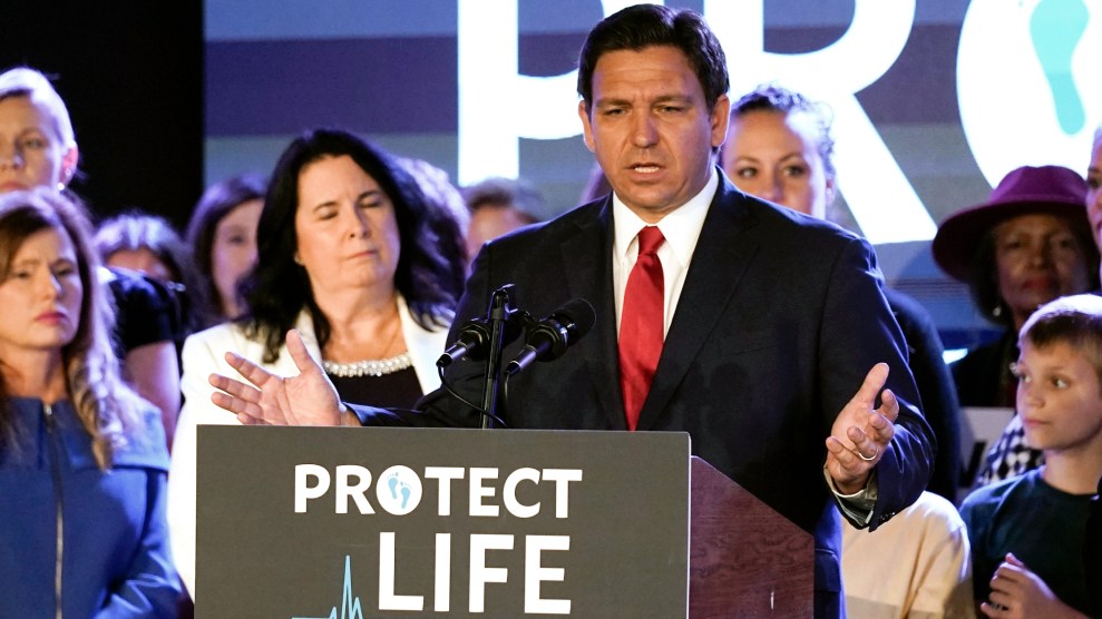 Ron DeSantis stands with his arms raised in front of a podium that says "Protect Life"