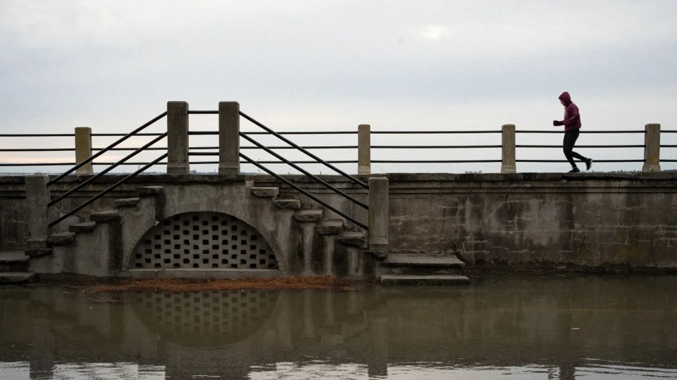 Dark water flows up to a set of concrete stairs and a raised grey concrete walking path. A silhouetted figure walks on the edge of the path.