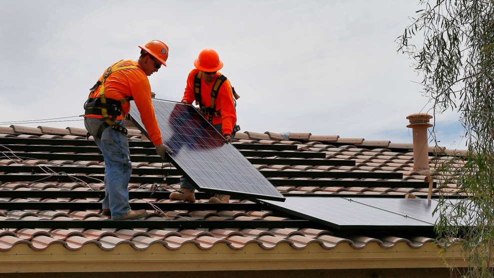 Two individuals wearing bright orange shirts and hats place a solar panel on a grooved roof.