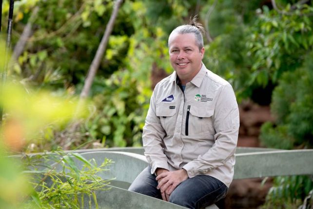 A white man, Peter Kyne, with graying hair sitting down at a bench outside smiling