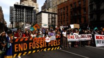 A group protests with a large banner saying "Biden End Fossil Fuels."