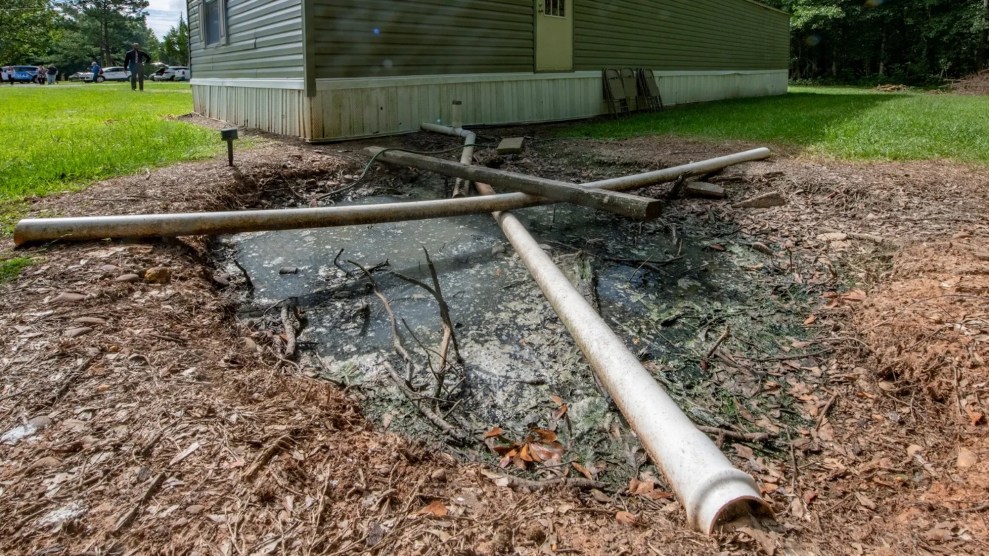 This shows sewage building up on the ground with some pipes over it, with a house in the background