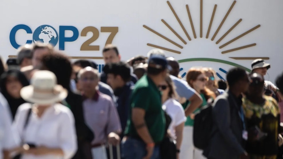 A crowd of people walk in front of a wall that says COP27 in blue and tan.