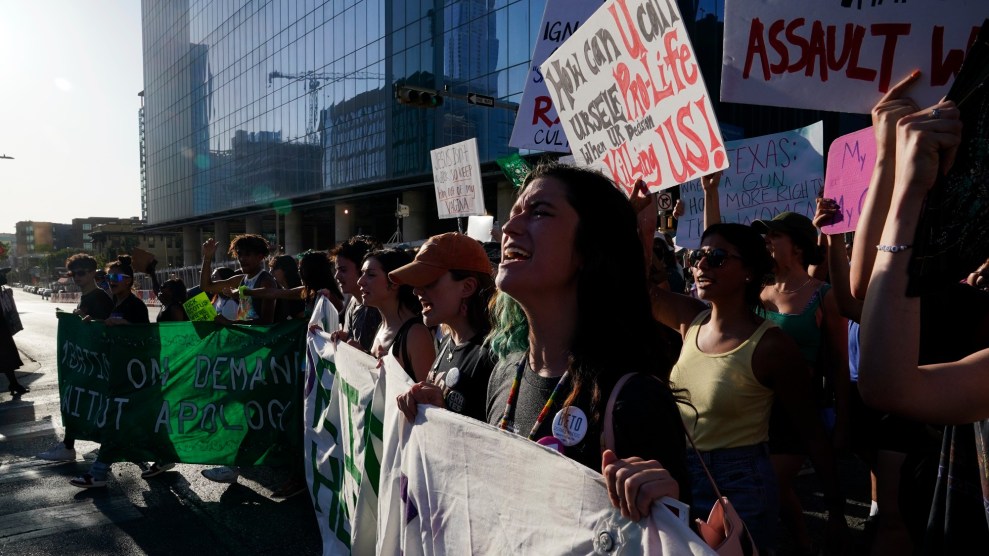 Protestors in Texas march through the street holding signs about abortion access. One protestor is in the foreground with an anguished expression.