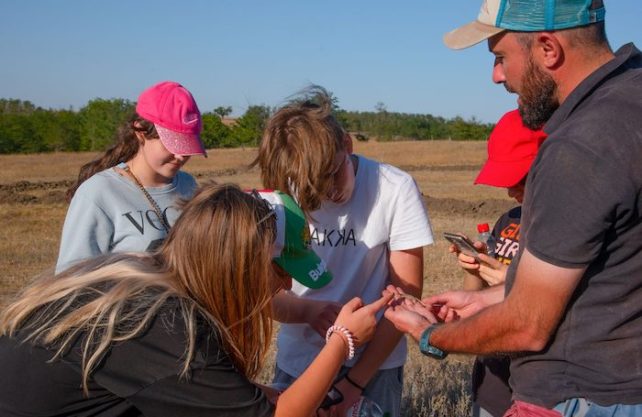 Four students gathered around a teacher outside, who is holding a small hamster