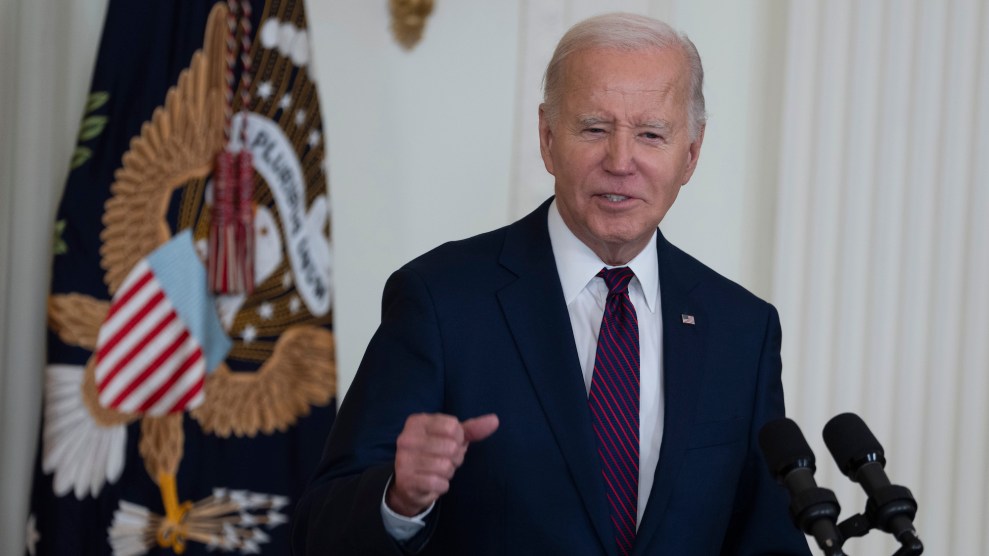 Joe Biden is a blue suit and blue and red tie speaking into black microphones