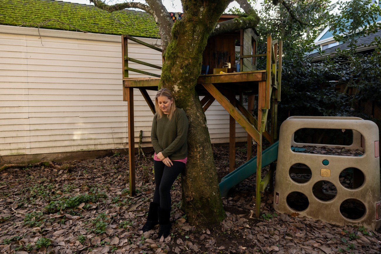 Woman standing against a tree, looking down.