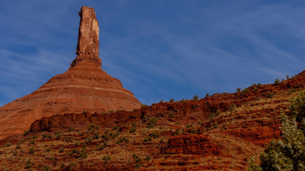 An orange rock formation speckled with green shrubs in front of a bright blue sky.