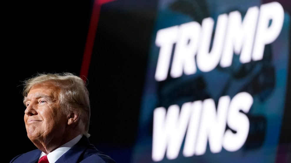 Donald Trump on a stage with a light up sign behind him that says "Trump Wins"