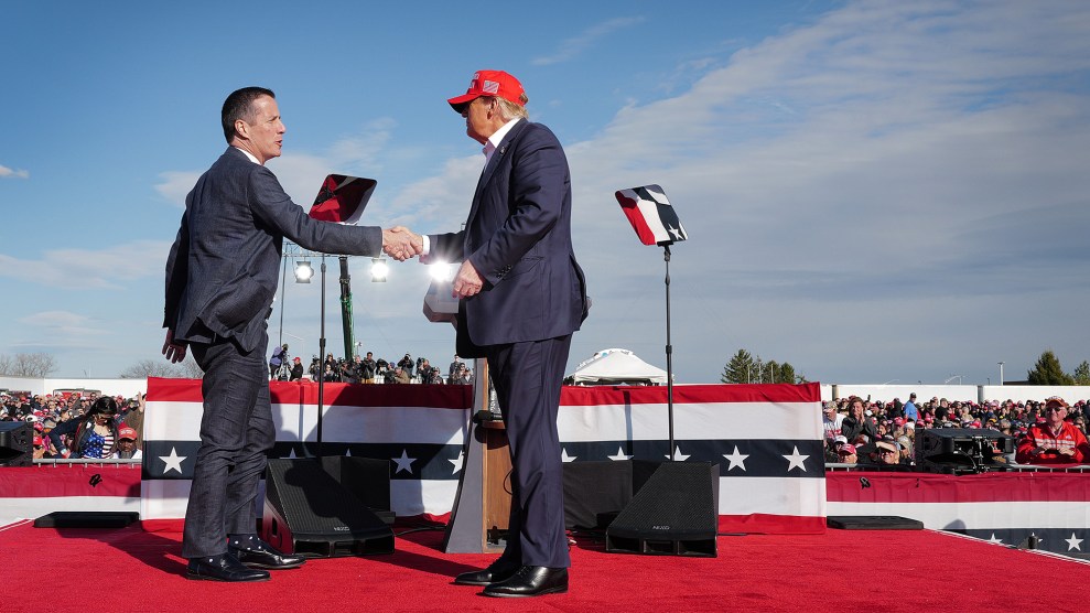 Donald Trump wearing a red hat on stage shaking a man's hand.