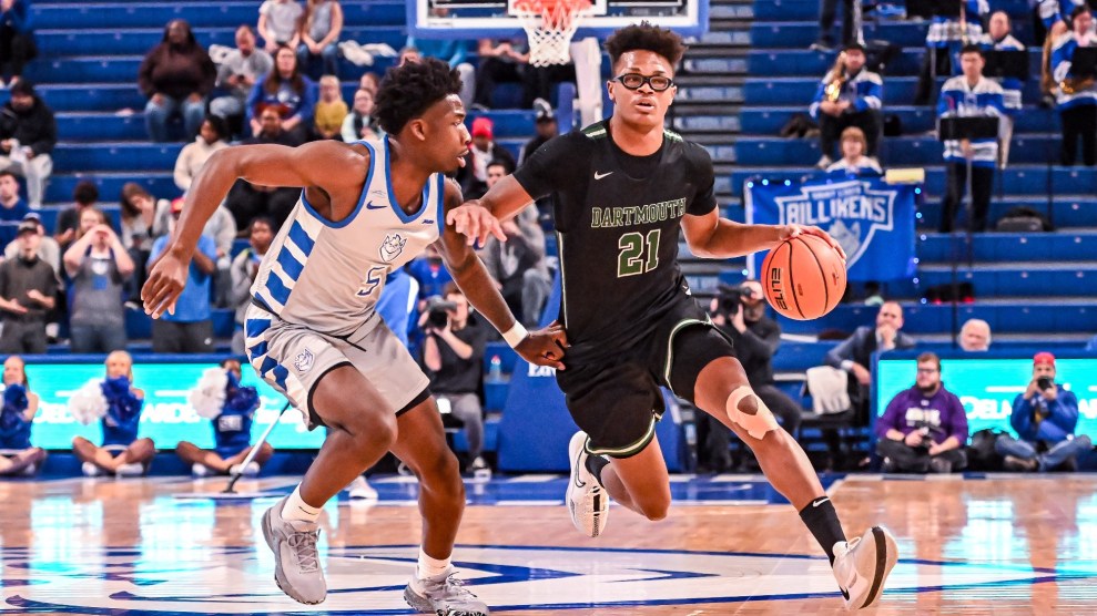 Basketball player on court poses mid-dribble while defending opponent.