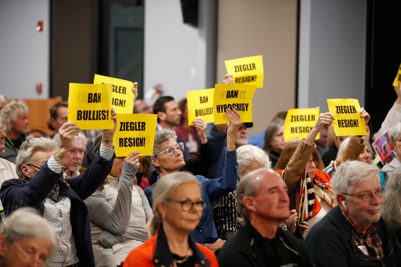 People hold up yellow signs that read, "Ban Bullies" and "Ziegler Resign!"