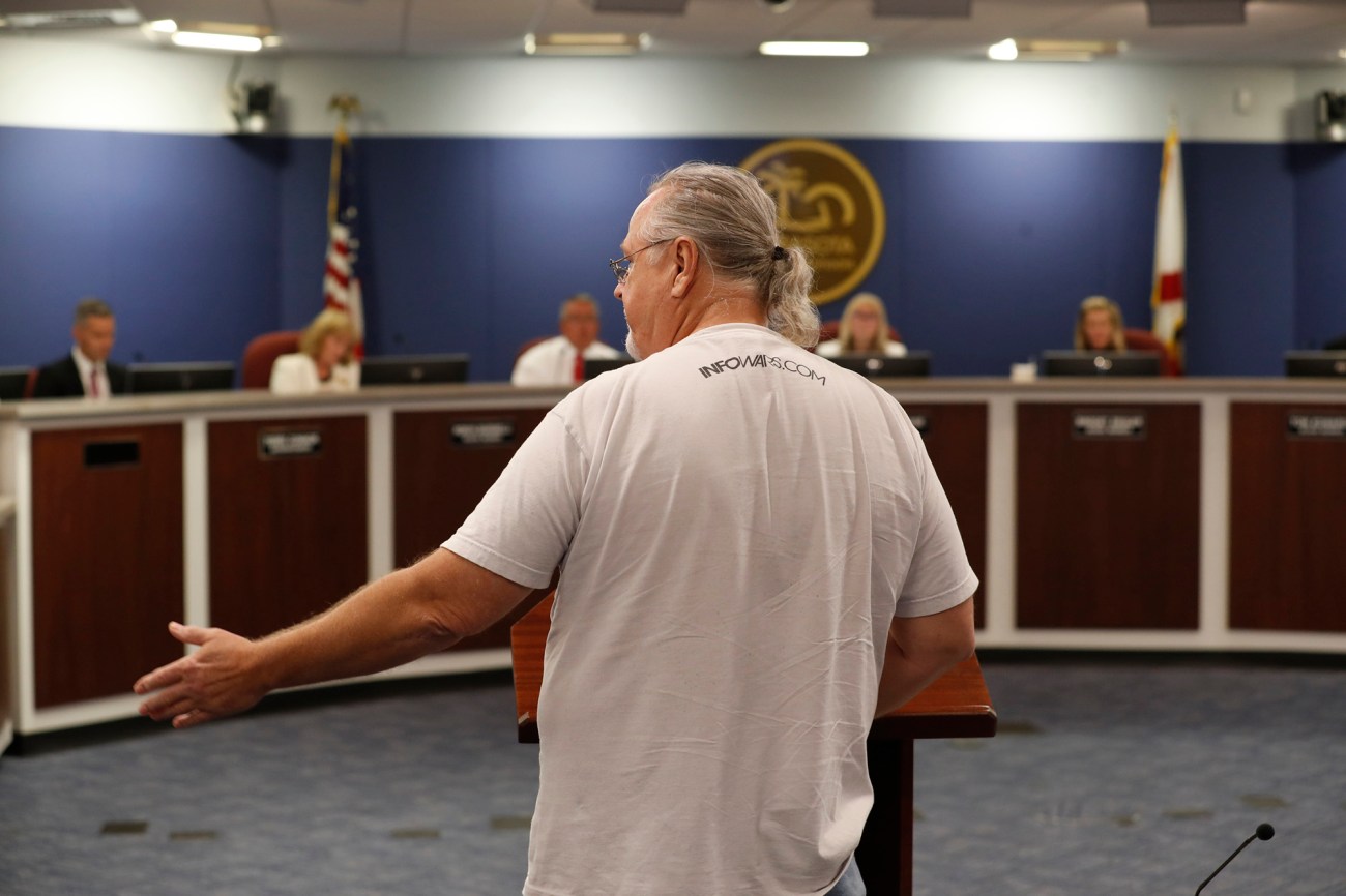 Man with ponytail and Infowars shirt addresses a school board meeting.