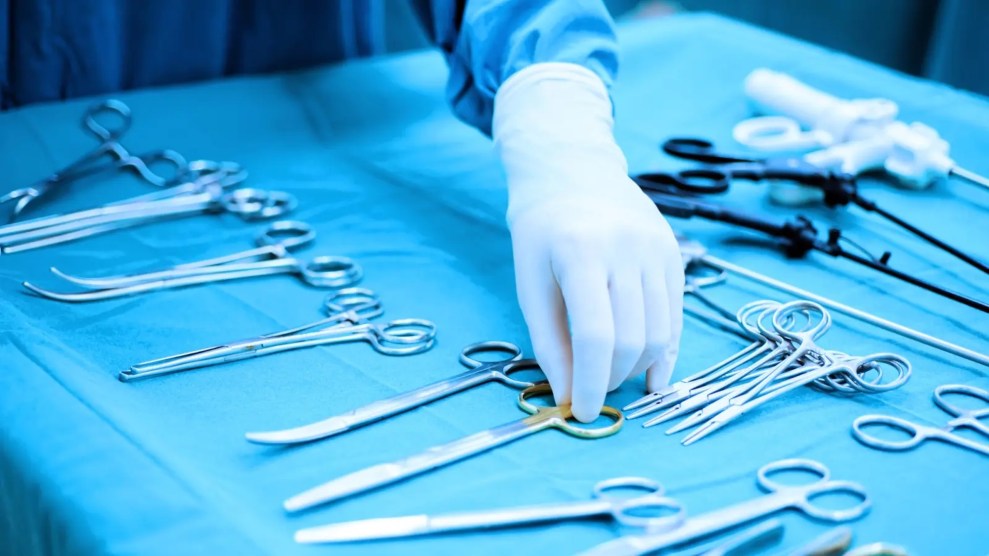 A gloved hands picks up scissors from a medical table