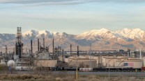 White-capped mountains tower above an oil refinery with an American flag painted on it.