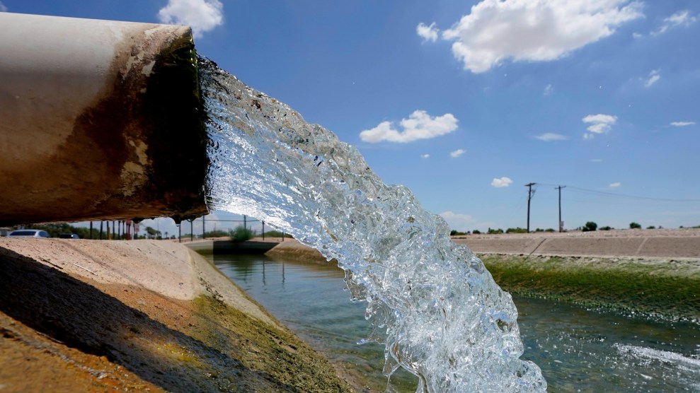 Water flows out of a pipe in front of a blue sky speckled with clouds.