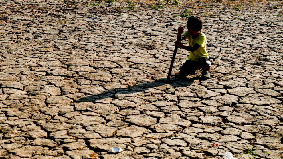 A boy bends over ground that is so dry cracks break through it.