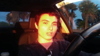 A young man sits at the wheel of his car.