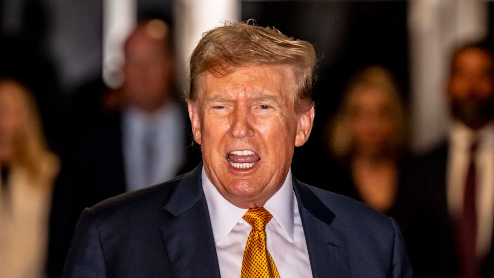 Donald Trump speaking with some people behind him, in a blue suit and yellow tie.