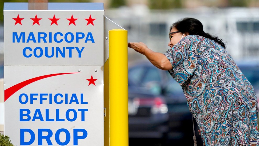 A woman in a dress dropping off a ballot at a box that says that says, "Maricopa County, Official Ballot Drop"