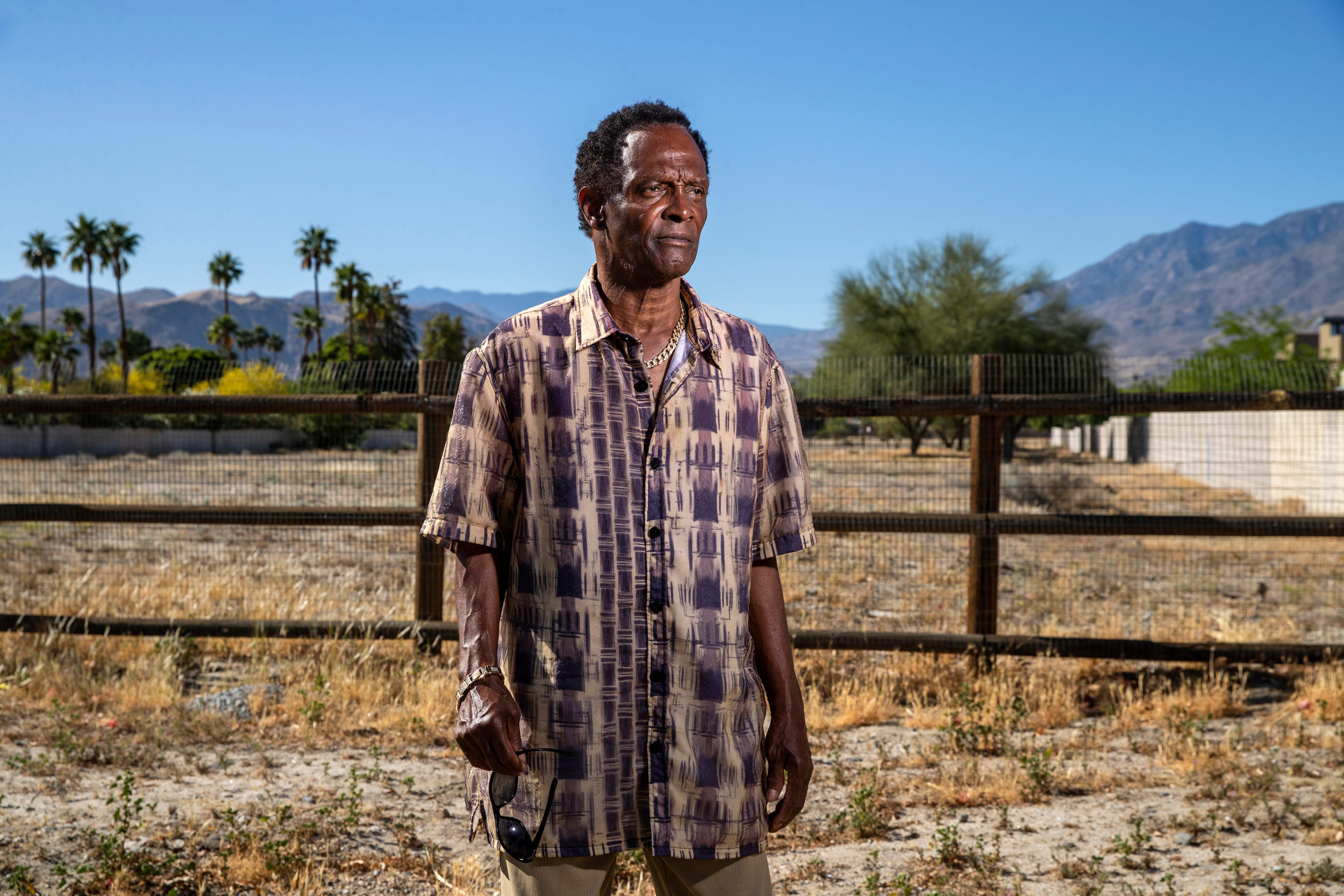 A man standing in front of an empty lot with a fence.