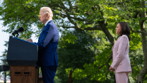 President Joe Biden stands at the presidential podium in the Rose Garden of the White House, as Vice President Kamala Harris stands a few steps behind him.