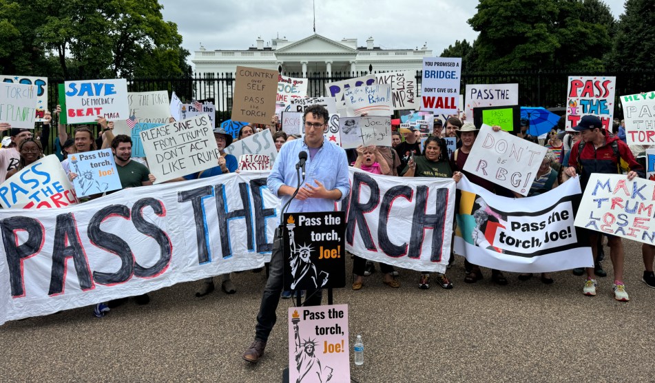 A large banner that says pass the torch behind a man speaking in front of the White House