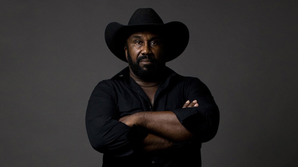 Portrait of black man wearing a black cowboy hat, with his arms crossed.