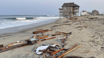 An unoccupied beach house that collapsed into the Atlantic Ocean from winds and waves caused by Hurricane Ernesto stands in the distance as debris litters the beach in the foreground.