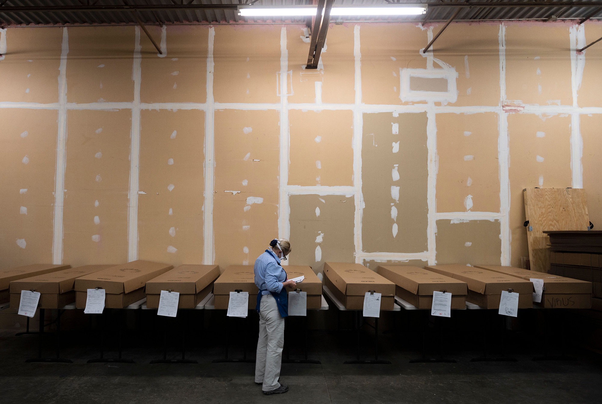 One person looking at a piece of paper in a large room filled with cardboard caskets.