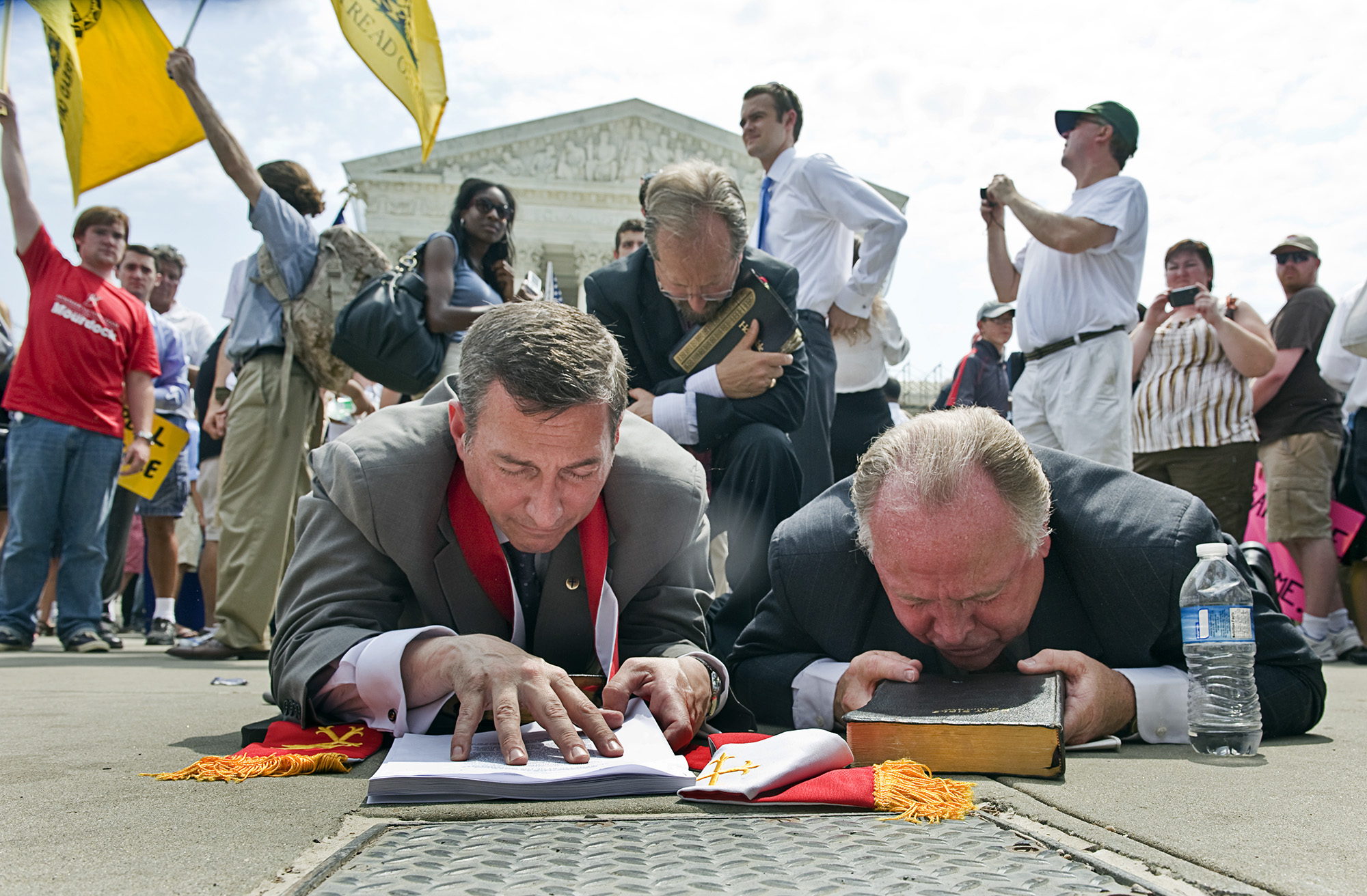 Two men laying down in front of the Supreme Court, praying with a group of people surrounding them.