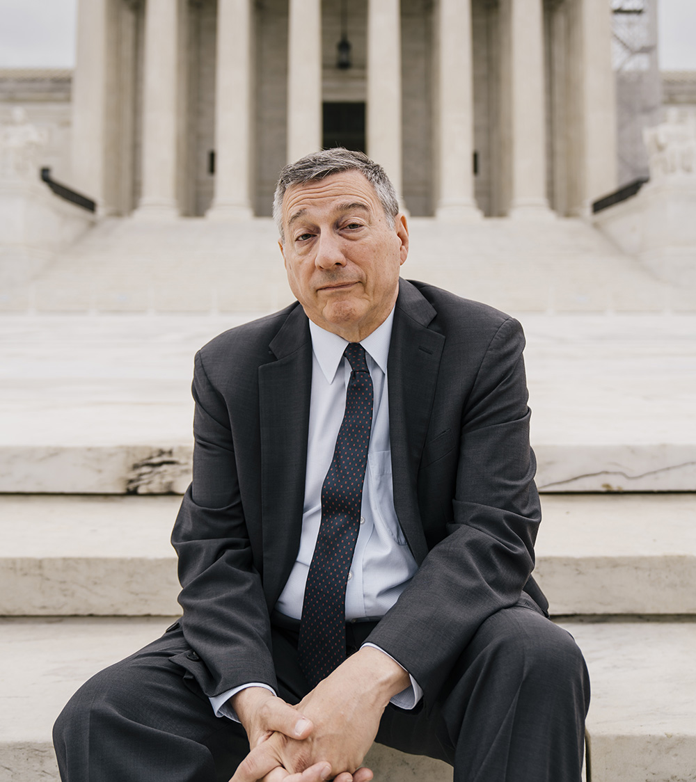 A man in a suit and tie sitting on steps in front of the United States Supreme Court