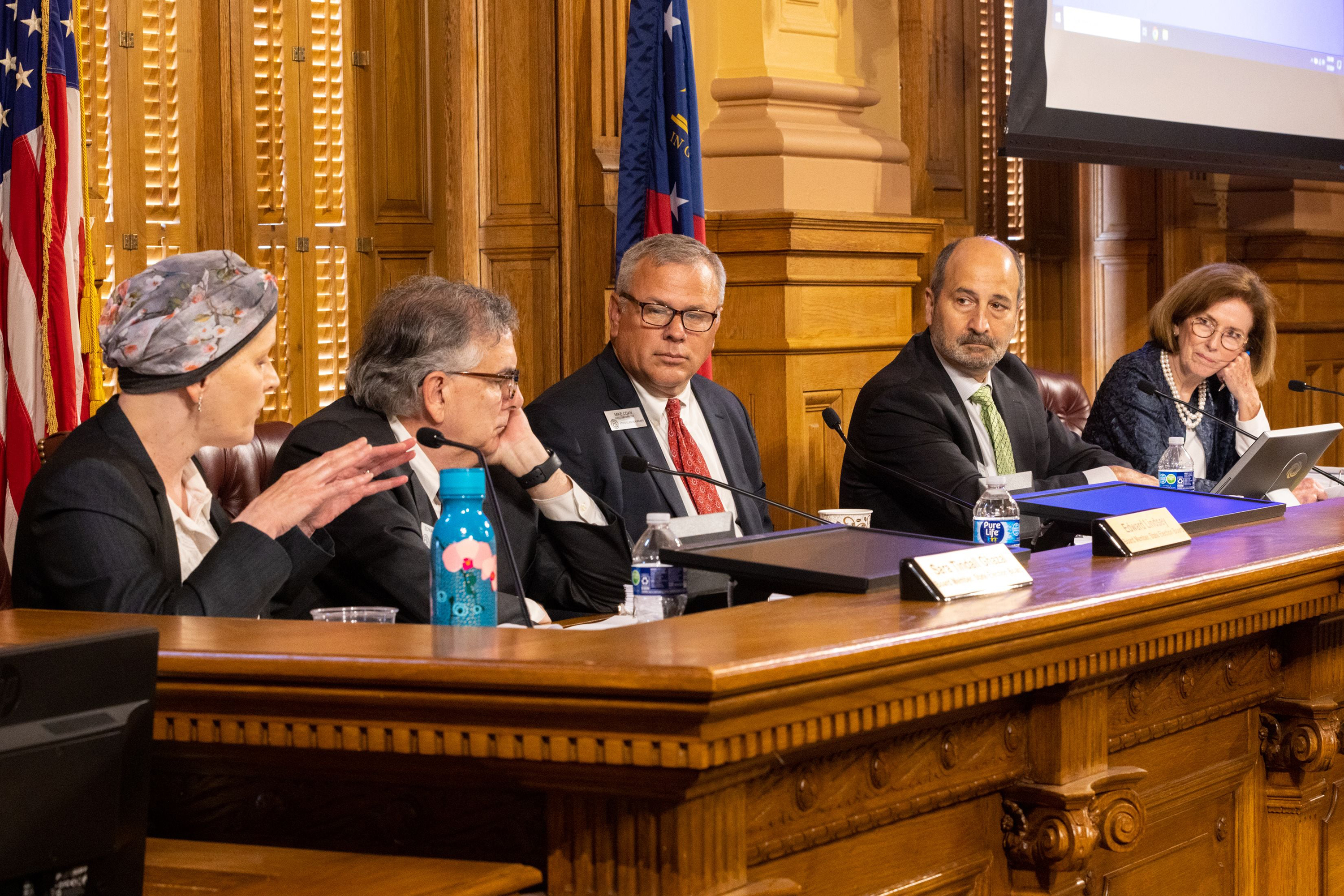 Group of people sitting at a long desk at a meeting.