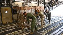 Three airmen push a pallet of boxes into an airplane's cargo hold.