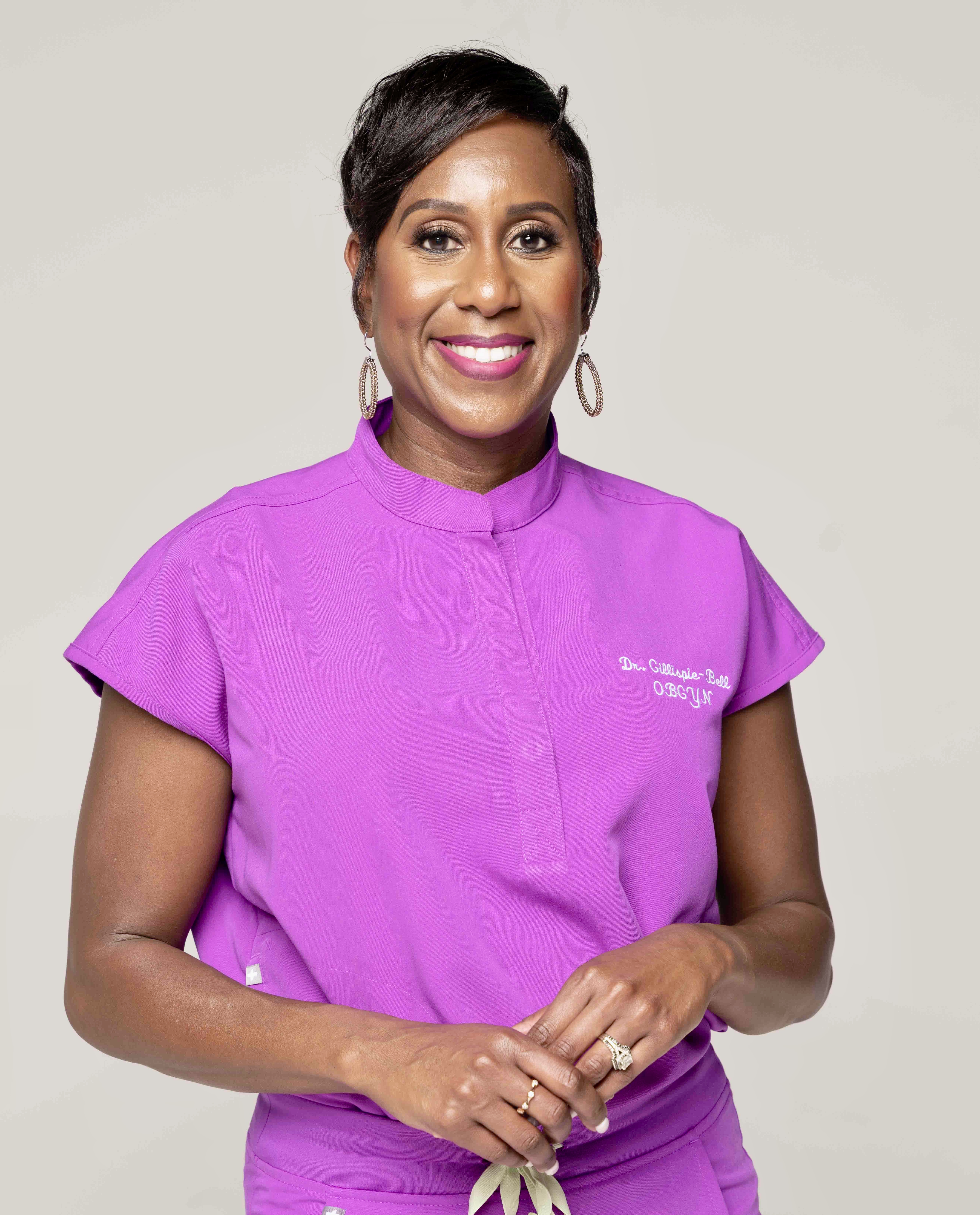 A portrait of Dr. Veronica Gillispie-Bell smiling in purple short-sleeve scrubs.