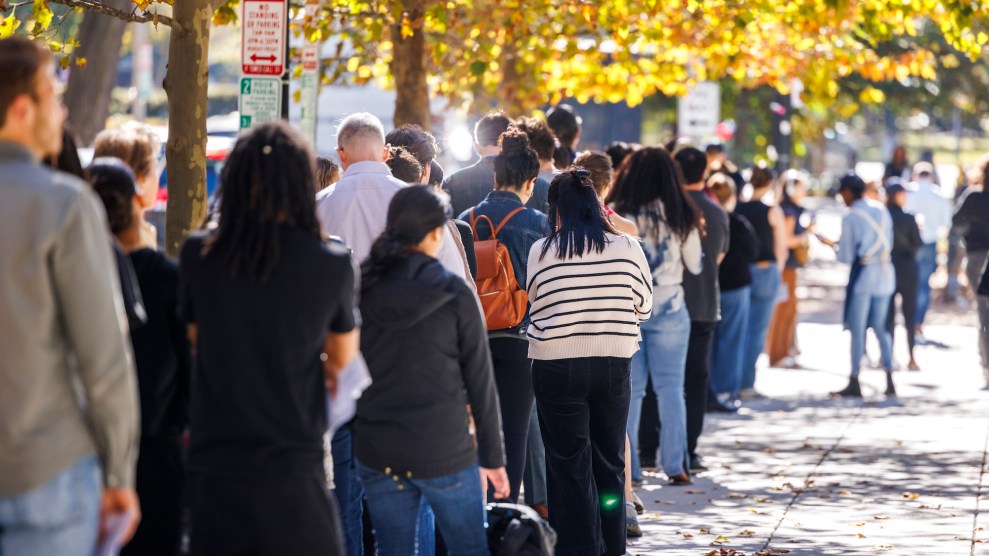 A group of people standing in a long line outside, with them facing away from the camera