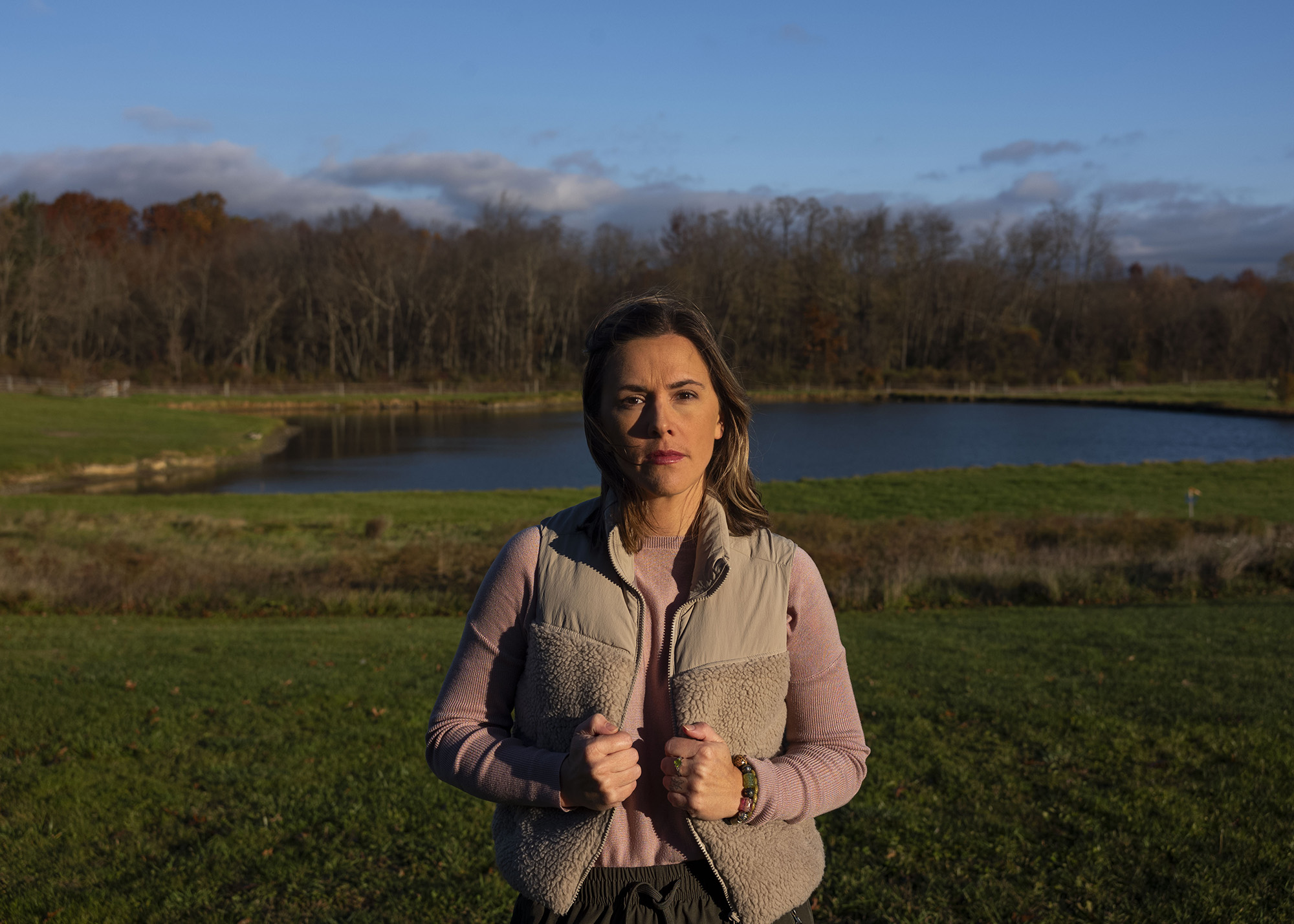 Portrait of a woman in a jacket standing by a pond.