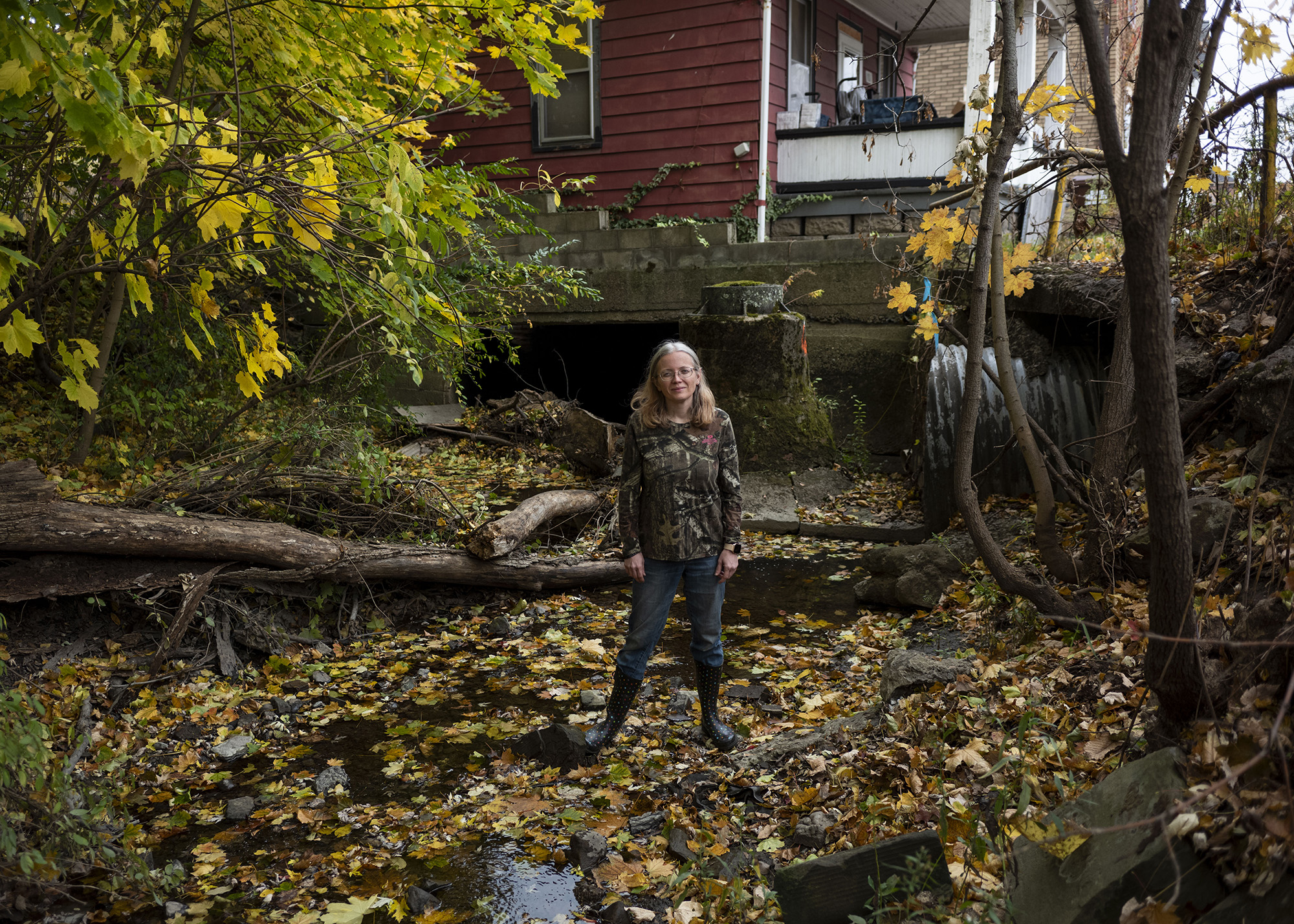 Woman standing in a creek amid foliage outside a house.