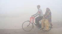 Two people on a bike are partially visible through thick air pollution