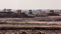 Four bulldozers on cleared land, in front of dusty sky.