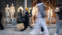 Blurred figures walk past sale signs.