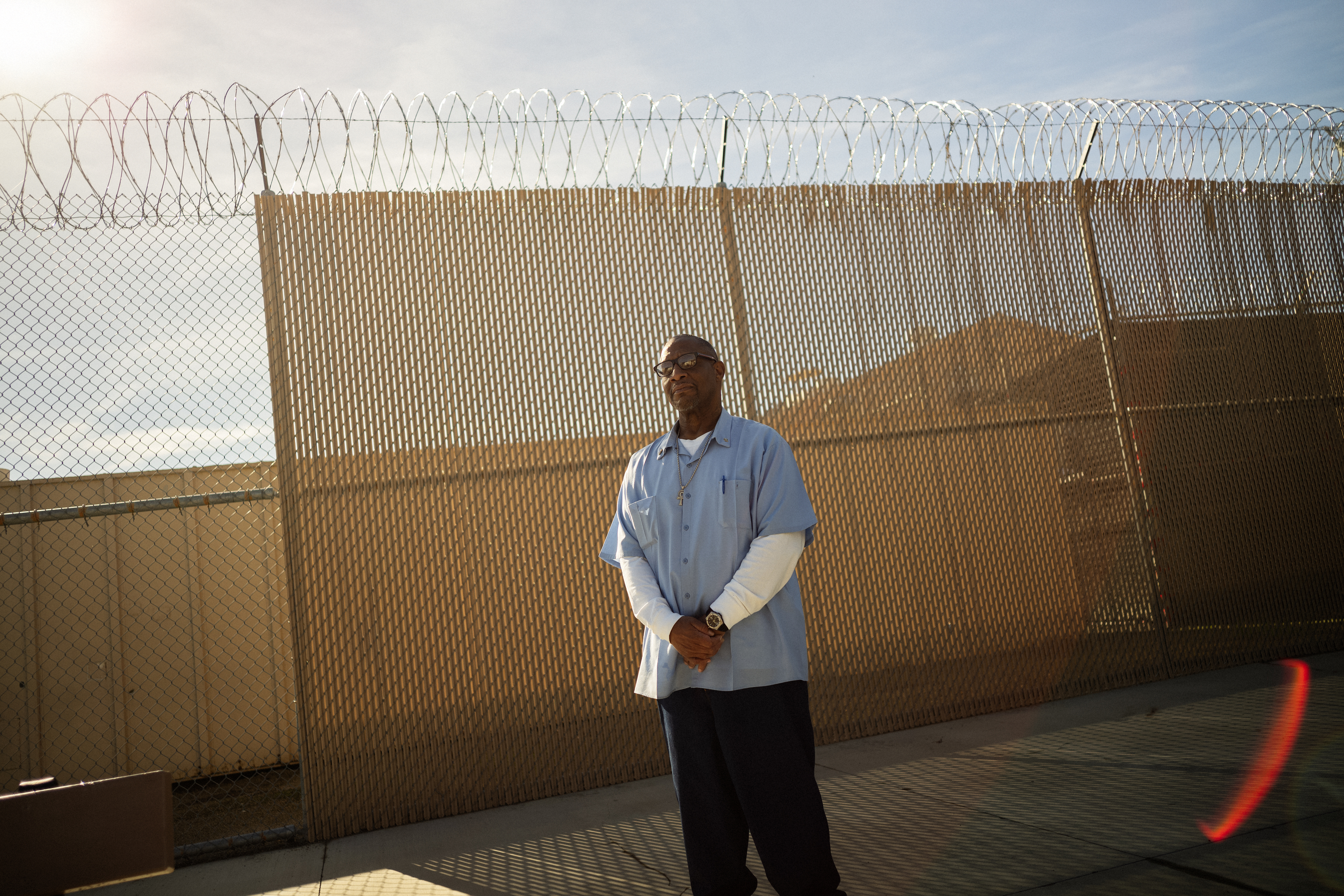 A man stands in a prison yard with his hands clasped in front of him.