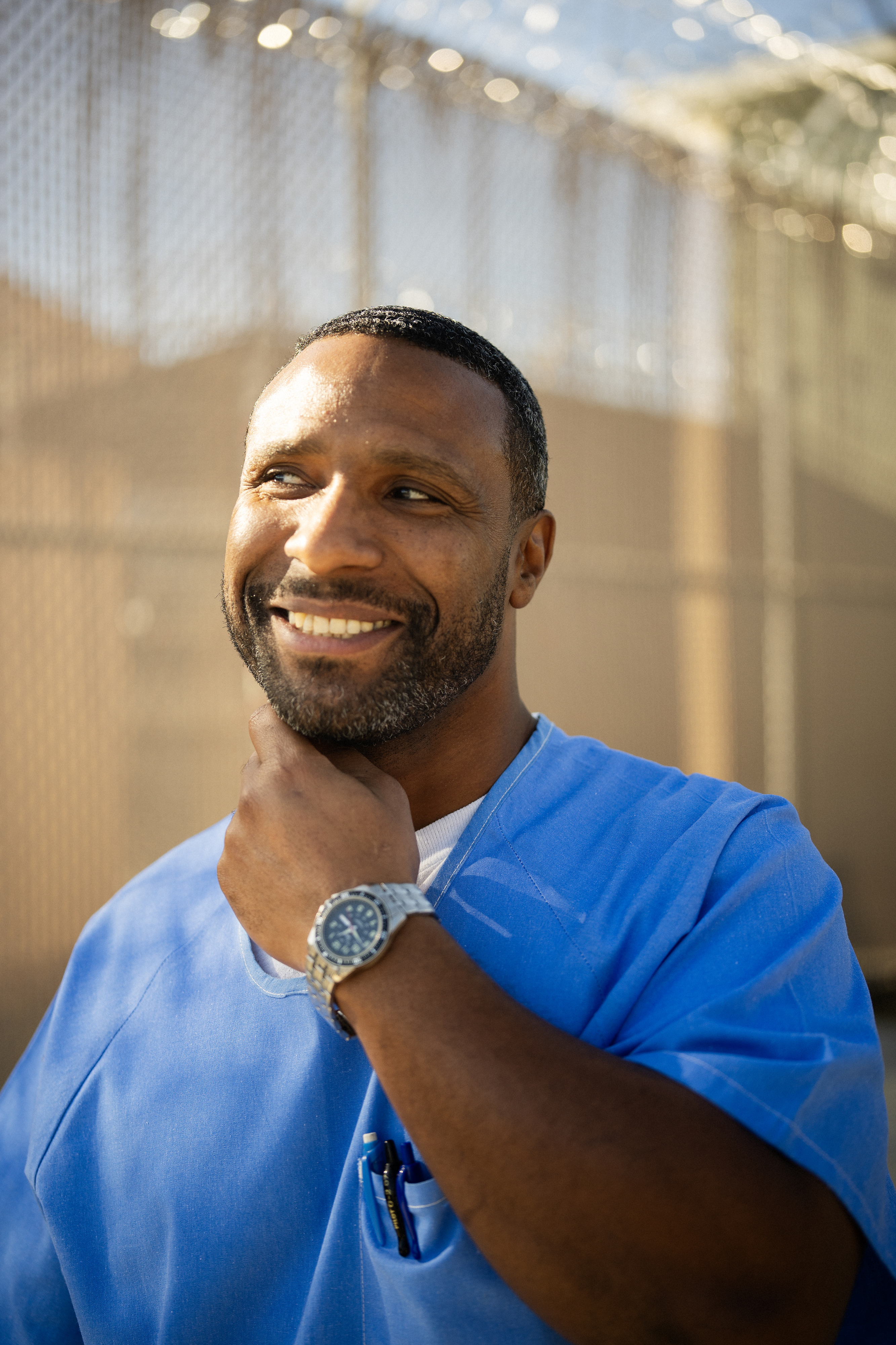 Portrait of smiling Black man wearing blue with his hand touching his neck.